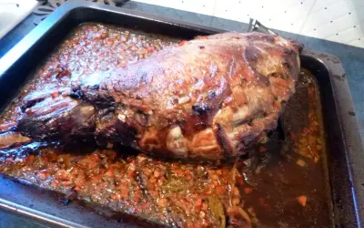 Gigot de sanglier rôti 7h, baignant dans son jus avec des légumes coupés. Un plat savoureux prêt à être dégusté.