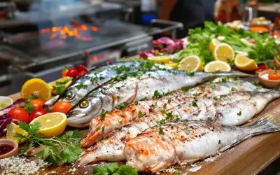 Poissons entiers et filets prêts pour le barbecue, accompagnés de citrons, tomates et herbes fraîches. Un délice en perspective !