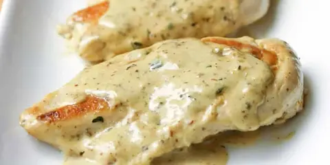 Deux morceaux de poulet à la crème, nappés d'une sauce onctueuse aux herbes, sur une assiette blanche. Un délice !