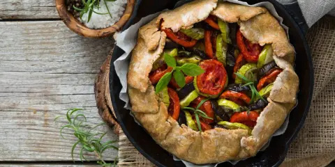 Tarte aux légumes colorée, garnie de tomates, courgettes et aubergines, prête à être dégustée.