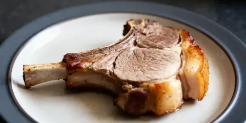 Une côte de porc dorée et juteuse, prête à être dégustée, repose sur une assiette.