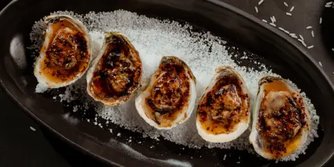Cinq huîtres au barbecue, grillées et savoureuses, servies sur un lit de gros sel.