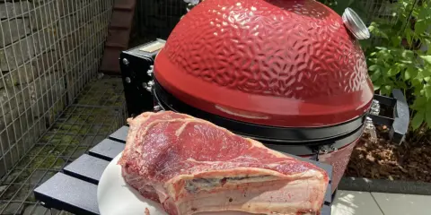 Une belle côte de bœuf crue attend sur une assiette blanche, prête à être grillée sur le barbecue rouge vif.
