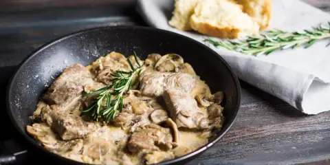 Délicieux sauté de porc crémeux aux champignons, garni de romarin frais, servi dans une poêle avec du pain croustillant à côté.