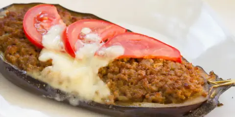 Aubergine farcie à la viande hachée, gratinée au fromage et garnie de rondelles de tomate. Une recette savoureuse et réconfortante.