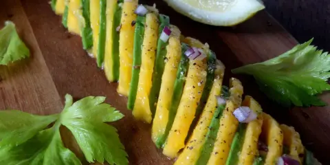 Une belle recette avocat et mangue, assaisonnée d'oignon rouge et de poivre, sur une planche en bois.