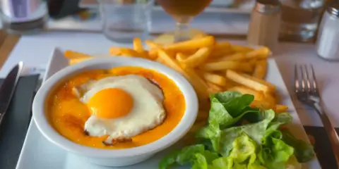 Un plat savoureux avec un œuf au plat sur une sauce orangée, des frites dorées et une salade verte. Un vrai délice, on se demande d'où vient le welsh !
