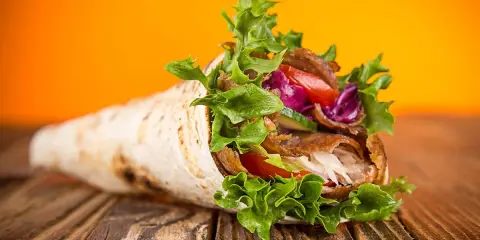 Un délicieux kebab maison garni de viande, salade croquante, tomates et chou rouge, sur un fond orange vif.