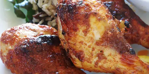 Trois pilons de poulet grillés et dorés, servis avec du riz et une tranche de citron.