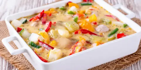 Un gratin de légumes coloré et crémeux, avec des poivrons, courgettes et autres légumes dans une sauce onctueuse, prêt à être dégusté.