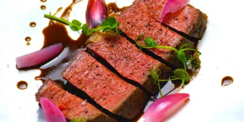 Une succulente entrecôte de bœuf, tranchée et nappée d'une sauce riche, accompagnée de jeunes pousses et d'oignons rouges marinés.