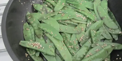 Pois gourmand croquants saupoudrés de graines de sésame dans une poêle.