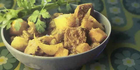 Un bol de colombo de porc, plat épicé aux morceaux de viande et de légumes, garni de coriandre fraîche.