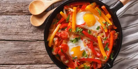 Poêlée de poivrons, tomates et œufs, une recette de piperade savoureuse, garnie de persil frais.