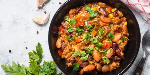 Un bol de chili sin carne, garni de persil frais, avec des haricots rouges, du maïs et des poivrons. Parfait pour un repas réconfortant.