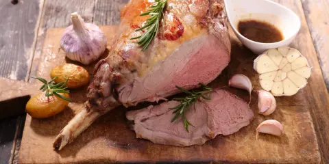 Gigot d'agneau rôti, servi avec des pommes de terre, de l'ail et une sauce. Une recette gastronomique qui met l'eau à la bouche.