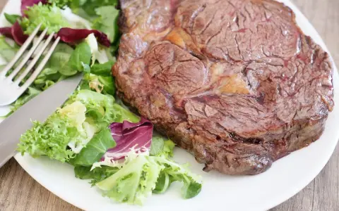 Une belle côte de bœuf juteuse, prête à être dégustée, accompagnée d'une salade fraîche. Parfait pour préparer un repas savoureux.