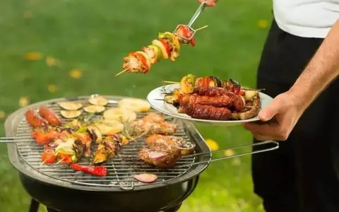 Un homme prépare un barbecue avec des brochettes et des saucisses. Qui a inventé le barbecue ? Mystère !