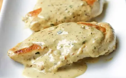 Deux morceaux de poulet à la crème, nappés d'une sauce onctueuse aux herbes, sur une assiette blanche. Un délice !