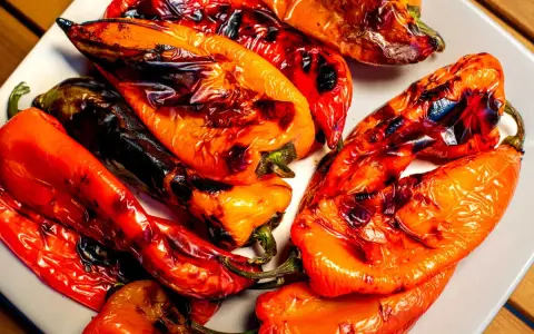 Poivrons rouges et orangés grillés au barbecue, légèrement noircis par la cuisson, sur une assiette blanche.