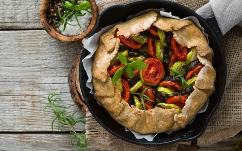 Tarte aux légumes colorée, garnie de tomates, courgettes et aubergines, prête à être dégustée.