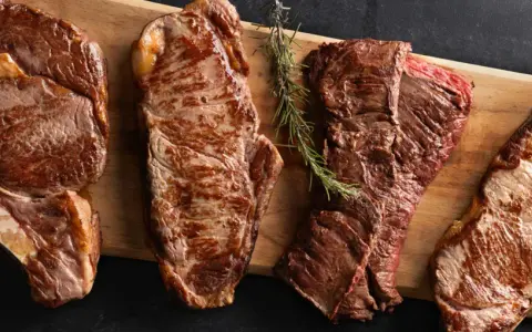 Quatre pièces de viande de saison octobre, grillées à la perfection, sur une planche en bois avec des herbes et du sel.