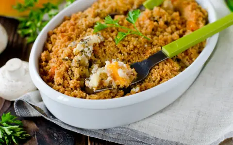 Un délicieux crumble salé aux légumes et riz, servi dans un plat blanc, avec une fourchette verte prête à déguster.