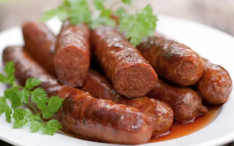 Assiette de merguez au four, dorées et juteuses, garnies de persil frais. Un délice prêt à être dégusté.