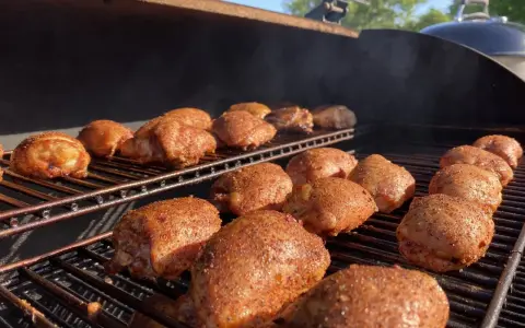 De nombreuses cuisses de poulet désossées, assaisonnées et grillées, fument sur un barbecue par une journée ensoleillée.