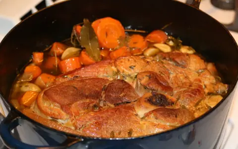 Rouelle de porc mijotant dans une cocotte avec des carottes, de l'ail et des herbes.