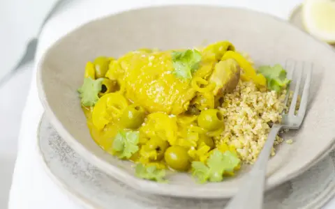 Un plat de tajine poulet citron, garni d'olives vertes et de coriandre fraîche, servi avec du couscous.