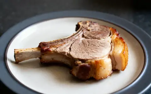 Une côte de porc dorée et juteuse, prête à être dégustée, repose sur une assiette.