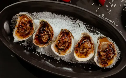 Cinq huîtres au barbecue, grillées et savoureuses, servies sur un lit de gros sel.
