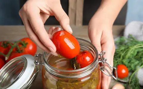Mains ajoutant une tomate dans un bocal pour une recette de tomate farcie le parfait.