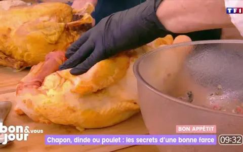 Main d'un cuisinier en gant noir préparant une farce poulet avec abats. Un chapon doré est à côté.