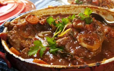 Un plat mijoté de veau marengo traditionnel, avec des morceaux de viande tendres dans une sauce tomate riche, garni de persil frais et de carottes.