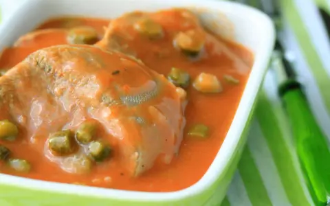 Tranches de langue de bœuf mijotées dans une sauce tomate onctueuse avec des petits pois. Un plat réconfortant servi dans un bol vert vif.