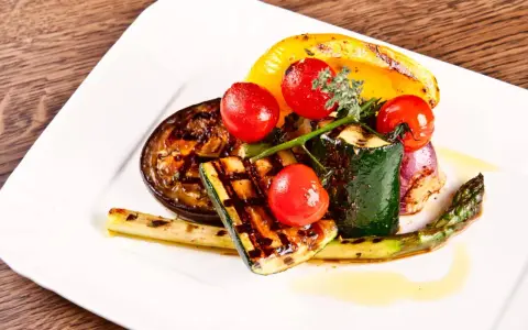 Légumes grillés : courgette, tomate, poivron jaune, aubergine, asperge et oignon rouge, arrosés d'une huile dorée.