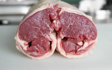 Un plat avec agneau cru, coupé en deux, révélant la chair rouge vif et le gras blanc. Prêt pour une cuisson savoureuse.