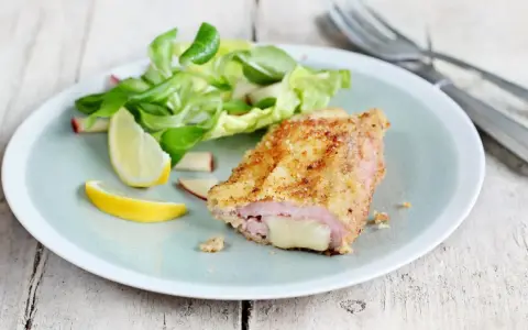 Un délicieux cordon bleu croustillant, garni de fromage fondant, servi avec une salade fraîche et des quartiers de citron.