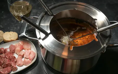 Préparation pour comment faire une fondue bourguignonne : morceaux de viande crue, pain et huile chaude dans le caquelon.