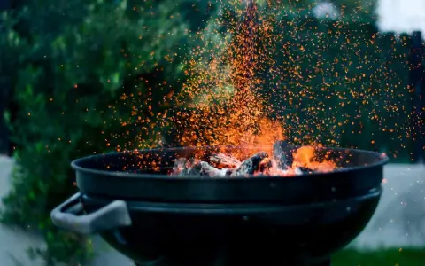 Un barbecue en plein air, avec des braises incandescentes et des étincelles qui dansent. L'odeur du barbecue bois ou charbon emplit l'air.
