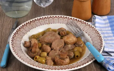 Un délicieux sauté de veau aux olives et champignons, servi dans une assiette décorée, prêt à être dégusté avec une fourchette bleue.