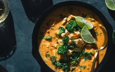 Un plat de poulet et brocolis baignant dans une sauce curry crémeuse, garni de quartiers de citron vert et de persil frais. Un délice !