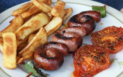 Assiette de saucisse à la plancha, frites dorées et tomates grillées. Un délice estival !