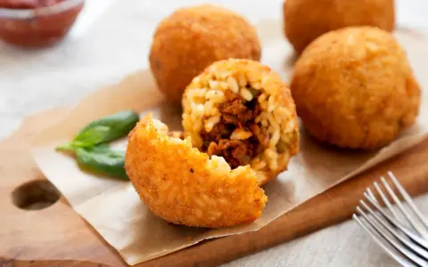 Arancini dorés et croustillants, un délice de la recette arancini, servis avec du basilic frais.