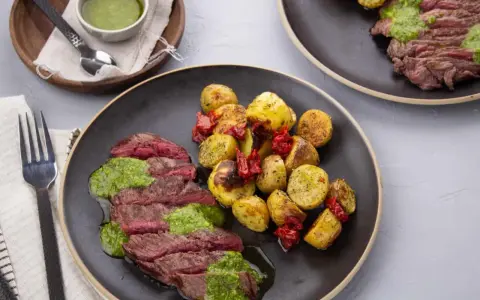 Tranches de bœuf juteux nappées de pesto, accompagnées de pommes de terre rôties et de tomates séchées. Quelle viande avec du pesto, un délice !