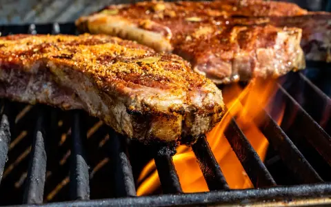 Deux entrecôtes savoureuses en cuisson sur un barbecue, les flammes dansent sous la viande.