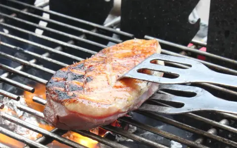 Magret de canard en cuisson indirecte sur un Weber, retourné avec une spatule. La peau est grillée et dorée, la chair rosée.