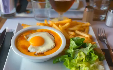 Un plat savoureux avec un œuf au plat sur une sauce orangée, des frites dorées et une salade verte. Un vrai délice, on se demande d'où vient le welsh !